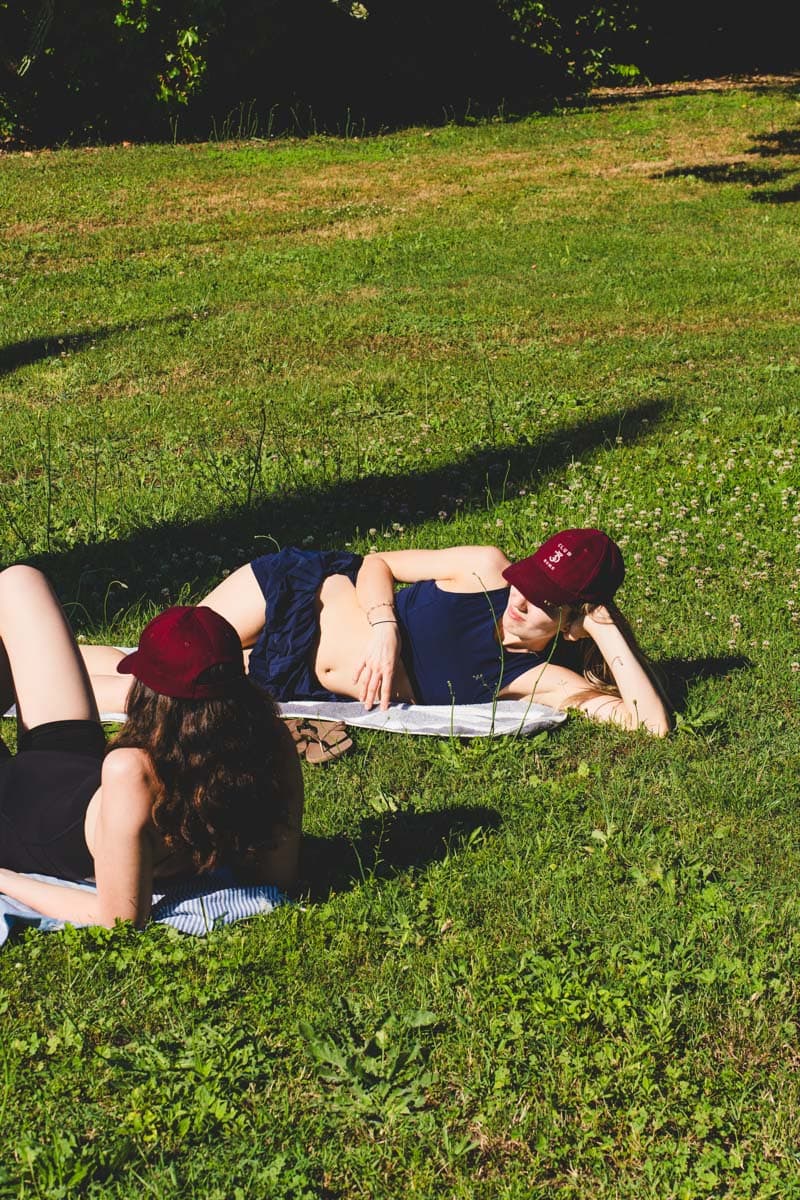 Due ragazze con i cappellini Club33 si rilassano sul prato dopo la lezione